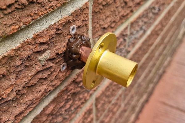 Brass outside tap being fitted to brick wall with brown silicone.