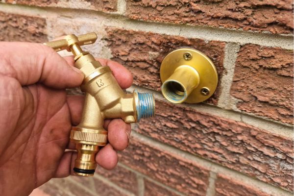 brass outside tap with liquid ptfe on threads being fitted onto brass wall plate