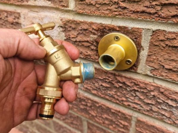 brass outside tap with liquid ptfe on threads being fitted onto brass wall plate